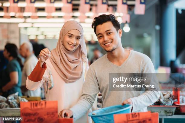 asian malay couple carrying a basket of prawn, picking up a prawn and looking at camera with smiling face during morning wet market shopping - malay lover stock pictures, royalty-free photos & images