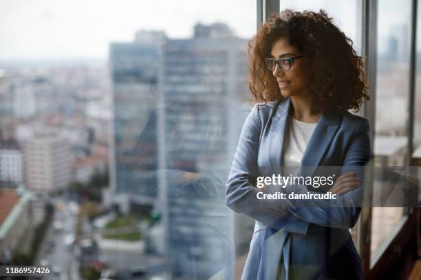 smiling thoughtful businesswoman looking through window - arab woman portrait stock pictures, royalty-free photos & images