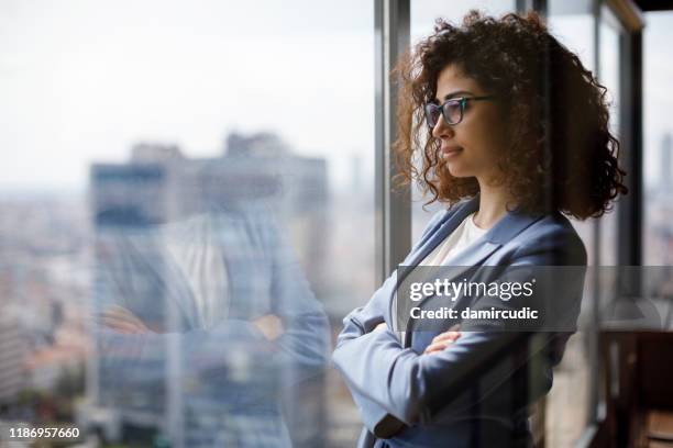 jeune femme d'affaires regardant par la fenêtre - city office photos et images de collection