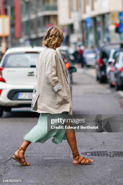 Guest wears a beige linen oversized jacket, a green side-slit skirt, brown leather gladiator flat sandals, outside the Sportmax show during Milan...