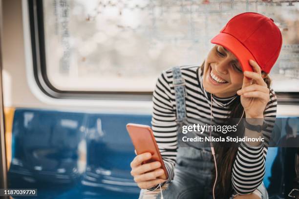 mujer sonriente escuchando música en el teléfono inteligente en el metro - gorra fotografías e imágenes de stock