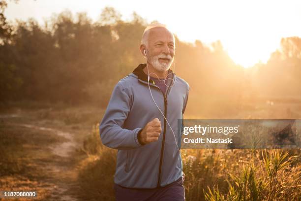 reifer mann joggt am morgen am see, fühlt sich wieder jung - laufen und gras und sport stock-fotos und bilder