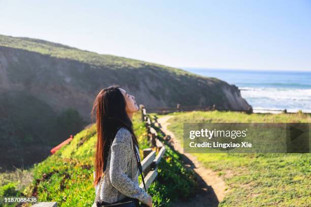 young woman standing along cliff coastline of pacific ocean, california - san mateo california stock pictures, royalty-free photos & images