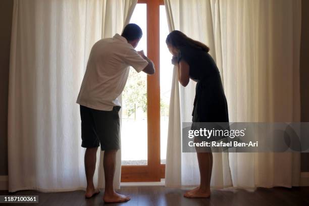 couple looking out from a window behind curtain - two people looking at view stock pictures, royalty-free photos & images