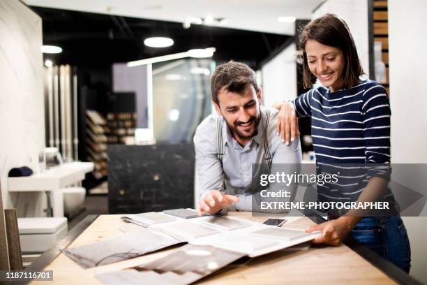 a woman leaning on the shoulder of her partner as they're looking at tile samples in a ceramics shop - choose stock pictures, royalty-free photos & images