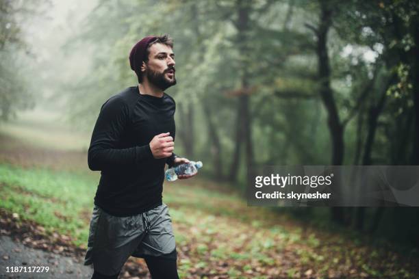 young athletic man running in autumn day at the park. - jogging winter stock pictures, royalty-free photos & images