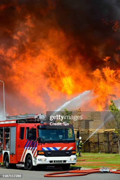 camión de bomberos frente a un gran incendio en una fábrica en una zona industrial - extinguir fotografías e imágenes de stock