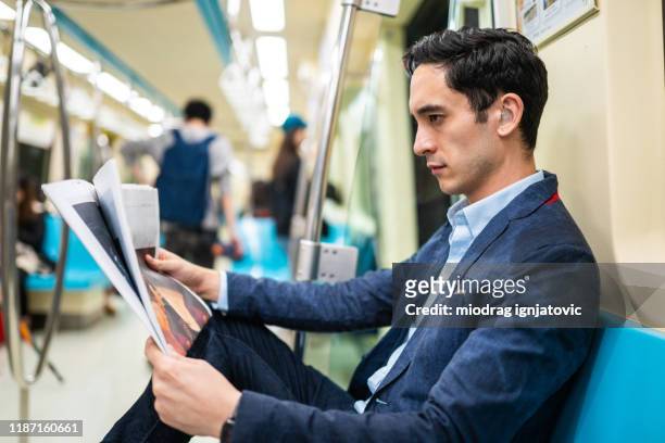 mixed race businessman reading newspaper on his way to work in train - hearing loss at work stock pictures, royalty-free photos & images