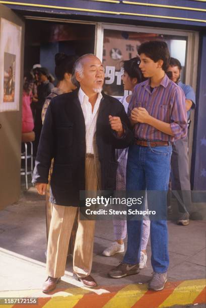 American actors Pat Morita and Ralph Macchio talk on the set of the film 'The Karate Kid Part II' , 1986. Also visible, between them, is...