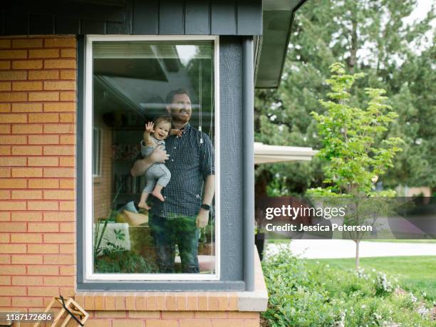 father holding his daughter behind window of house - utah house stock pictures, royalty-free photos & images