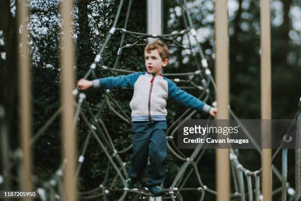 boy balancing on climbing frame looking to the side - touwbrug stockfoto's en -beelden