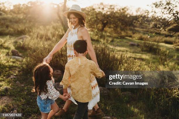 close up of mother in hat playing ring around the rosie with children - mexican american stock pictures, royalty-free photos & images