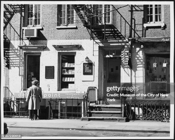 Woman stands outside a needlework and art gallery space next to the Oscar Wilde Memorial Bookshop at 15 Christopher Street, New York, New York, circa...