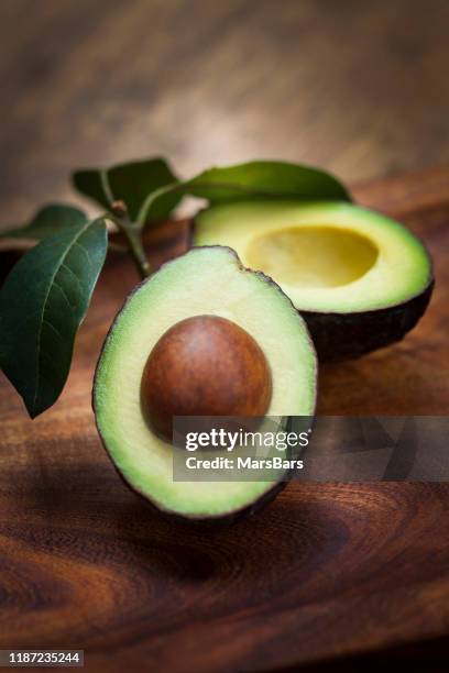 mitades de aguacate en tabla de madera con hojas - abocado fotografías e imágenes de stock