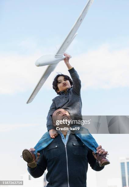 hispanischer vater und sohn fliegen spielzeugflugzeug - arm um schulter stock-fotos und bilder