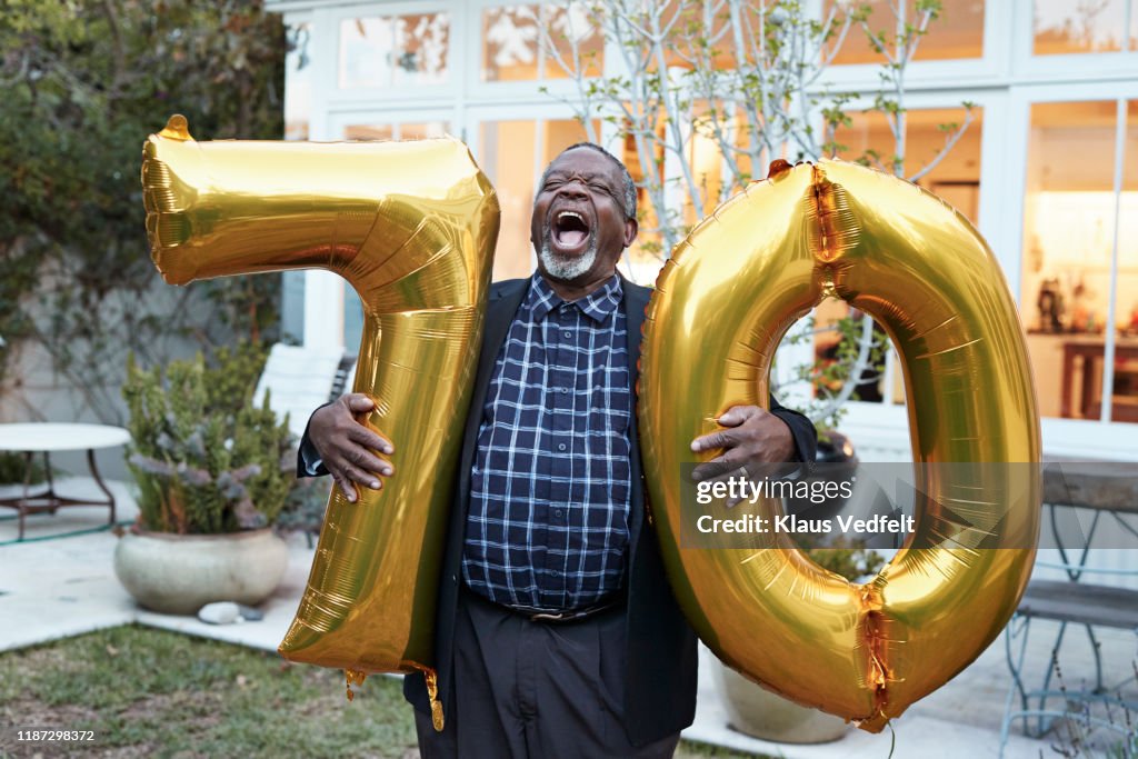 Man with number 70 balloons laughing in backyard