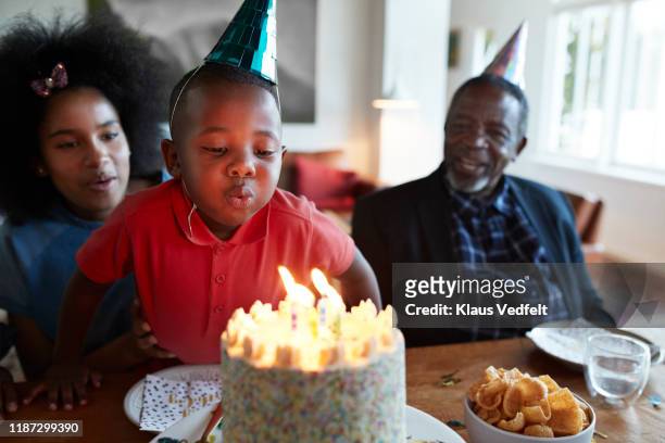 boy blowing candles on birthday cake at home - family moments stock-fotos und bilder