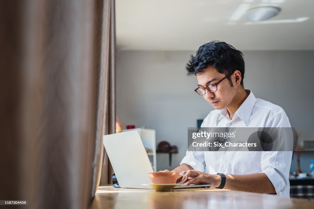 Joven hombre de negocios asiático trabajando con computadora portátil mientras se sienta en la cafetería de la cafetería