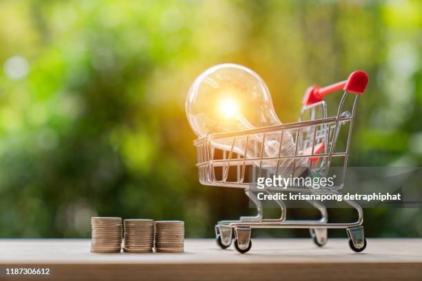 energy saving light bulb with stacks of coins and shopping cart for saving, financial and shopping concept. - consumerism foto e immagini stock