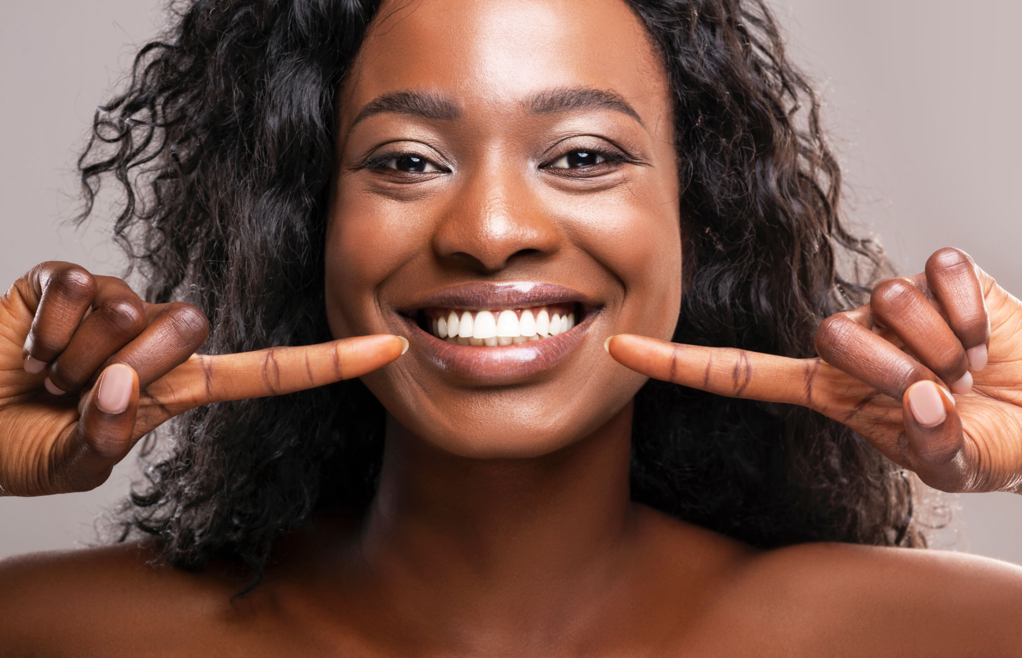Happy black woman pointing at her perfect white teeth Happy black woman pointing at her perfect white teeth