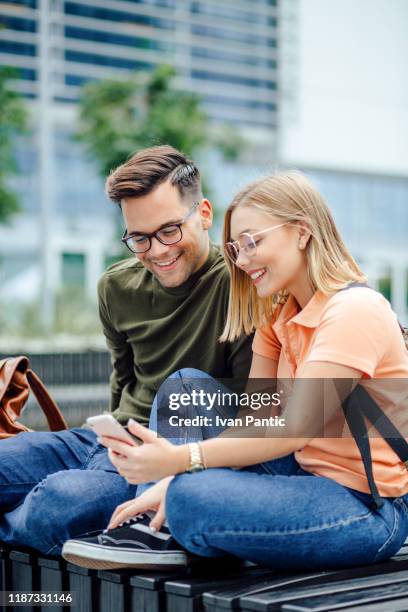 junges studentenpaar sitzt auf einer bank - bank student stock-fotos und bilder