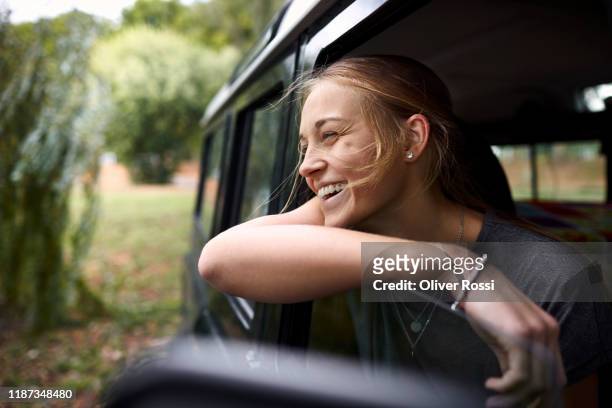 happy young woman looking out of car window - people in car stockfoto's en -beelden