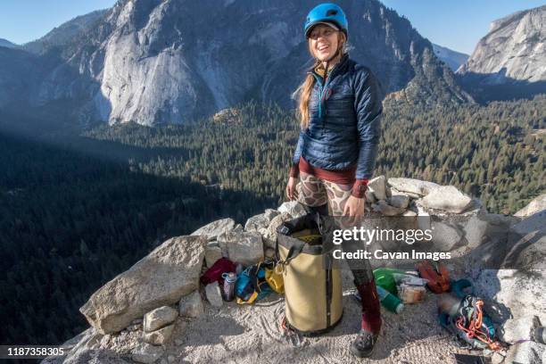 a young woman climber smiles as she stands on last night's bivy ledge - bivouac stock pictures, royalty-free photos & images