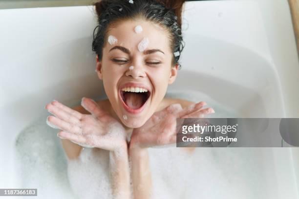 young beautiful woman is lying in the bathroom with foam and playing with foam and bubbles - taking a bath stock pictures, royalty-free photos & images