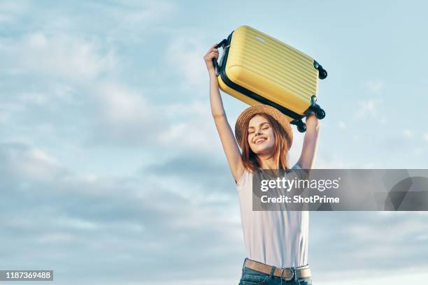 young beautiful and happy woman with a yellow suitcase on a background of clouds, travel - woman suitcase stock pictures, royalty-free photos & images