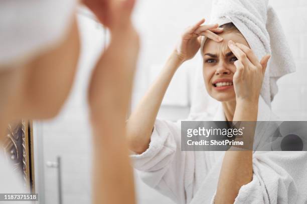 beautiful woman looks in the mirror and squeezes out a pimple, facial care - anti mask fotografías e imágenes de stock