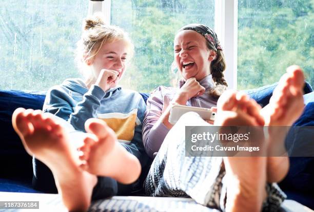 young girls sitting on a couch looking at a screen and laughing - smartphones dangling stock pictures, royalty-free photos & images