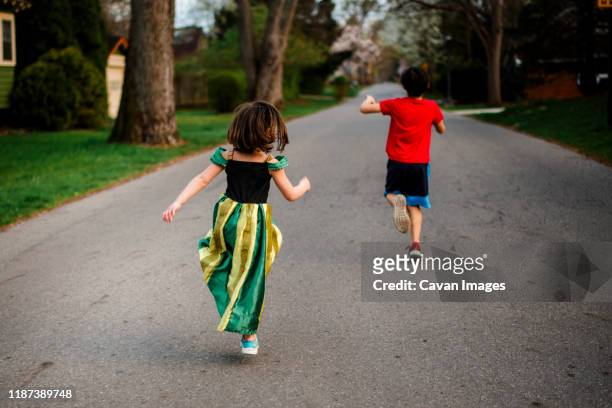 two children skip happily down a tree-lined street in springtime - skip stockfoto's en -beelden