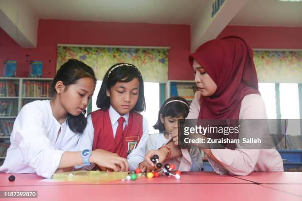 asian teacher in hijab holding a model of molecule while teaching elementary school students in science lab. - malaysia school stock pictures, royalty-free photos & images