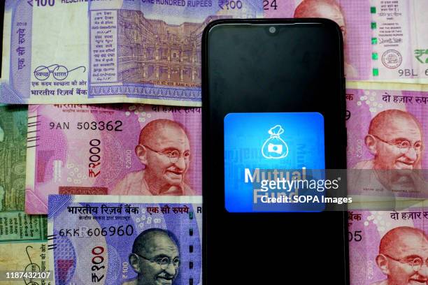 In this photo illustration a Mutual fund logo seen displayed on a smartphone with the Indian Currency Note One Hundred and Two thousand on the...