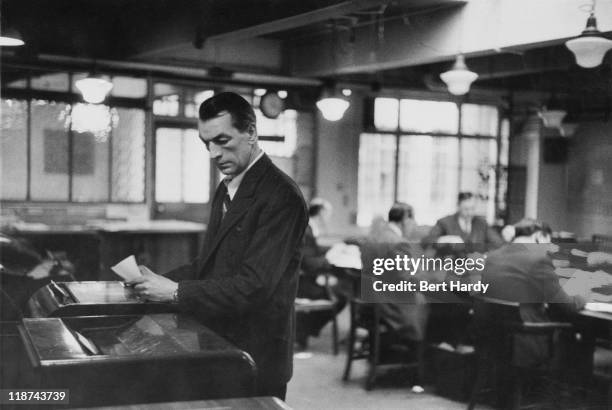 Sub-editors work at a table while material is taken off a tape machine on a Saturday afternoon in the newsroom at the offices of the News of The...