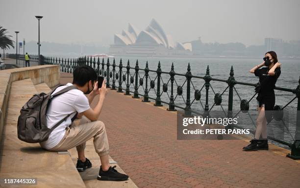 Tourists wearing masks take photos as the Opera House is enveloped in haze caused by nearby bushfires, in Sydney on December 10, 2019. Toxic haze...