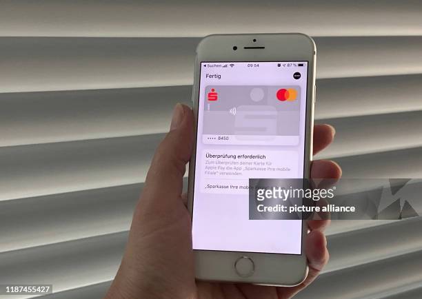December 2019, Berlin: A customer of the Hamburger Sparkasse holds a mobile phone in her hand and adds her credit card to the Apple Pay payment...