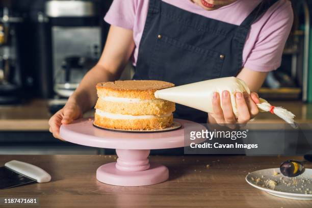 woman's hands in black apron decorate cake, squeezes out vanilla cream on a side of a cake - alcorza fotografías e imágenes de stock