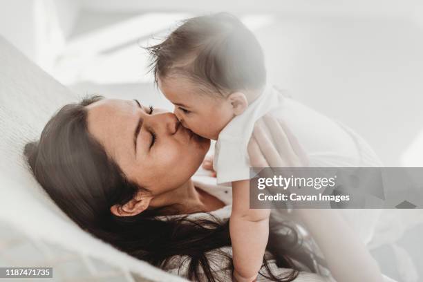 mother kissing baby daughter hammock in natural light studio - fond studio stock pictures, royalty-free photos & images