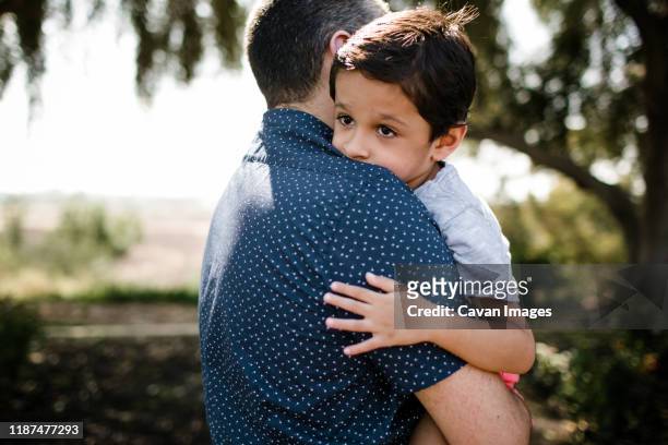 autistic boy hugging dad while standing under tree - autismus stock pictures, royalty-free photos & images