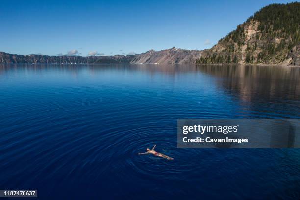 a young man swims in the cold, clear waters of crater lake. - crater lake stock pictures, royalty-free photos & images