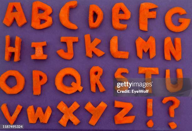 the alphabet cut out of carrots on a purple background - bubble font stock pictures, royalty-free photos & images