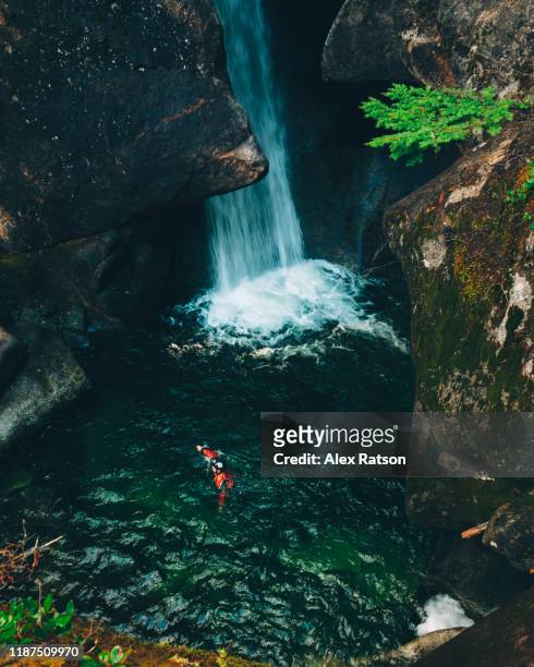 A Canyoneer swims across a waterfall fed pool deep with in a remote canyon