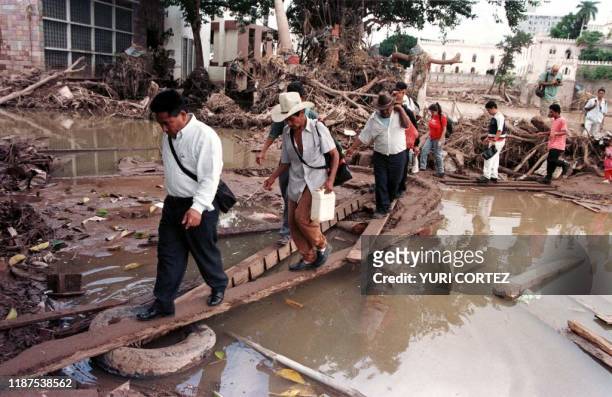Residents of Tegucigalpa use planks to cross standing water left after floods by Hurricane Mitch in the Honduran capital 11 November. An estimated...