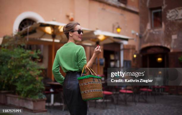 elegant woman walking on roman city street, holding basket - italian woman stock-fotos und bilder