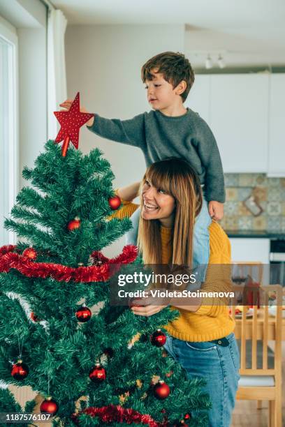 mutter und sohn setzen stern auf weihnachtsbaum - weihnachtsengel stock-fotos und bilder