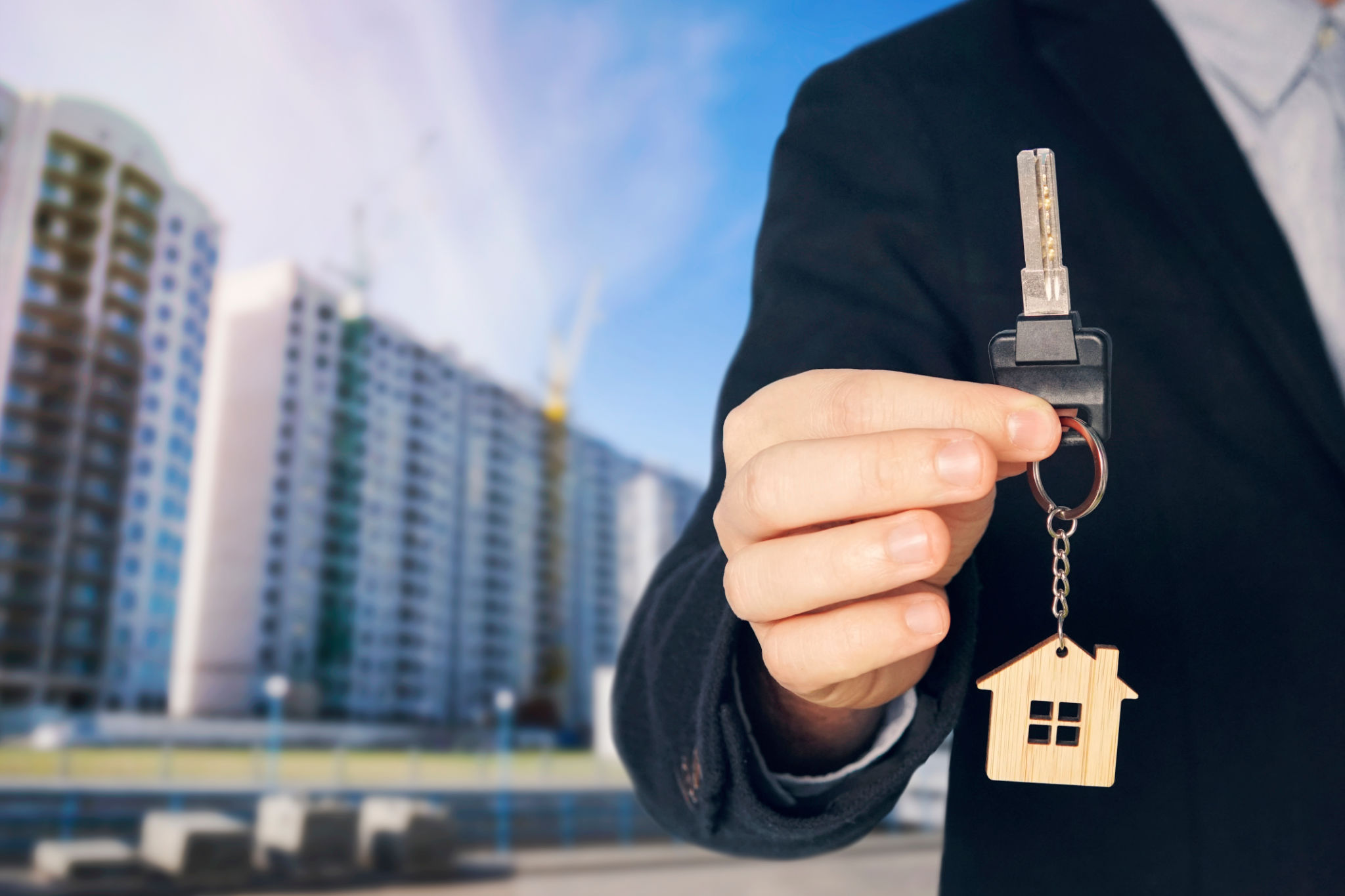guy in the suit shows me the keys. Key chain in the form of a house in a man's hand. Holding house keys on house shaped keychain in front of a new home. guy in the suit shows me the keys. Key chain in the form of a house in a man's hand. Holding house keys on house shaped keychain in front of a new home.