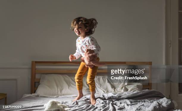 kleines mädchen springt auf ein bett - aufwachen stock-fotos und bilder