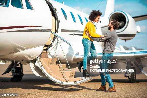 young rich woman putting hands on his partner's shoulders as she's getting ready to get out of a private airplane parked on an airport tarmac - extreme wealth stock pictures, royalty-free photos & images