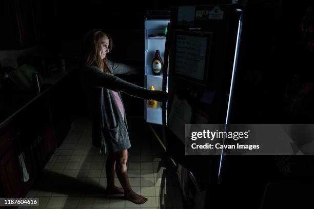 young adult woman in dark kitchen looks into open refrigerator - open fridge ストックフォトと画像